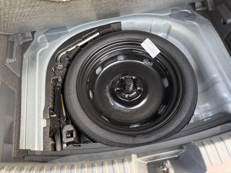 Vue plongeante sur la roue de secours noire et les outils de bord dans le coffre d'une SEAT LEON 1.5 eTSI Hybrid 2025.