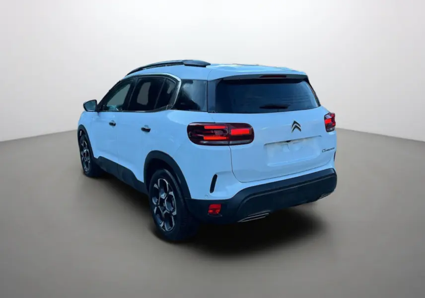 Vue 3/4 arrière droite d'un Citroën C5 Aircross blanc okénite avec barres de toit et vitres surteintées.