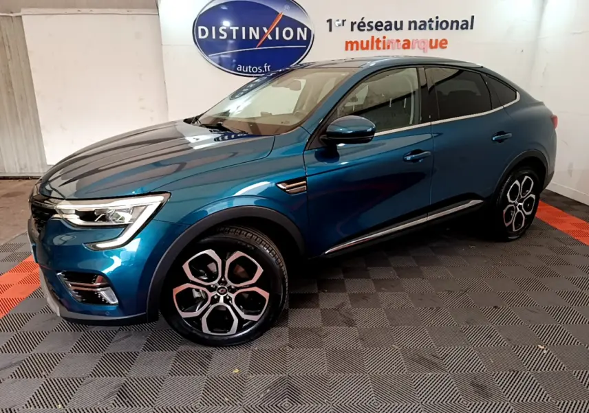 Renault Arkana Techno bleu en vue 3/4 avant droit, avec jantes distinctives et toit noir dans un showroom intérieur.