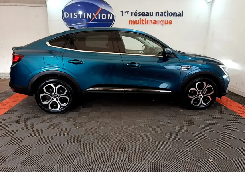 Profil droit d'une Renault Arkana Techno E-Tech bleu 2023 en hybride, avec jantes alliage distinctives et toit plongeant.