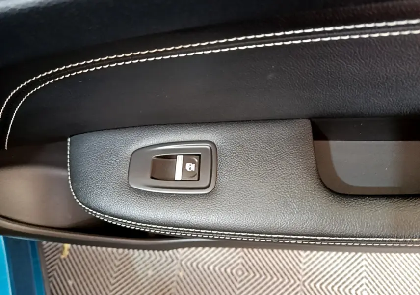 Gros plan sur la commande de verrouillage de porte noire avec surpiqûres blanches, intérieur d’une Renault Arkana bleu.