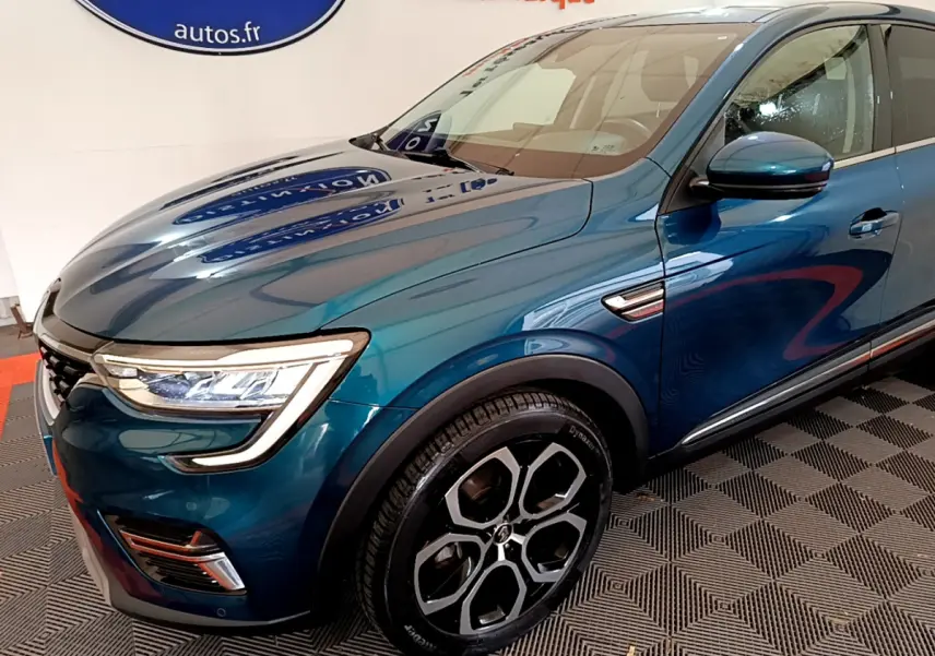 Vue 3/4 avant droit d'une Renault Arkana Techno E-Tech hybride bleu avec jantes noires et phares LED distinctifs.