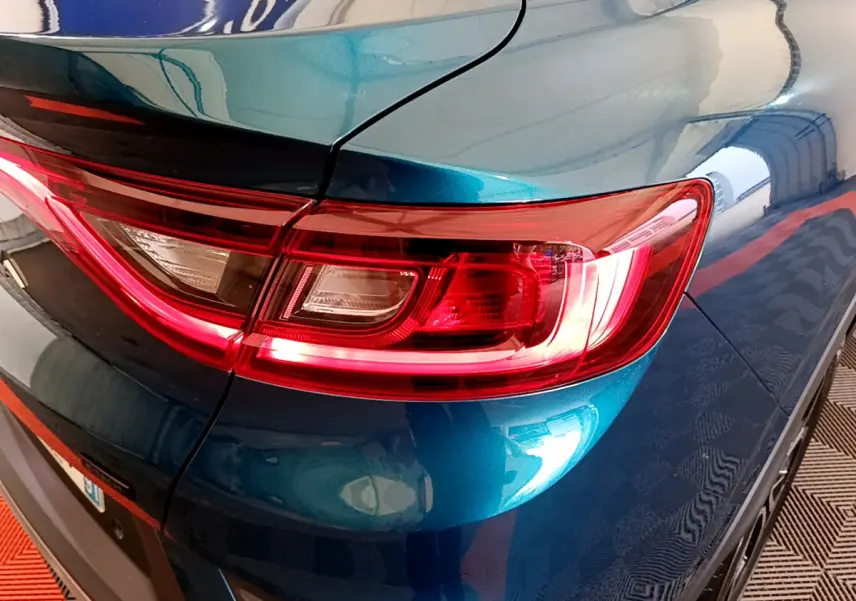 Gros plan sur le feu arrière droit rouge d’un Renault Arkana bleu métallisé 2023, avec reflet sur la carrosserie.