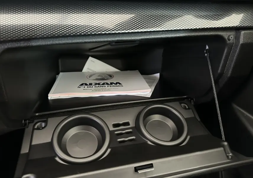 Gant de boîte à gants ouvert avec manuel utilisateur Aixam Ambition visible, intérieur noir sobre et fonctionnel.