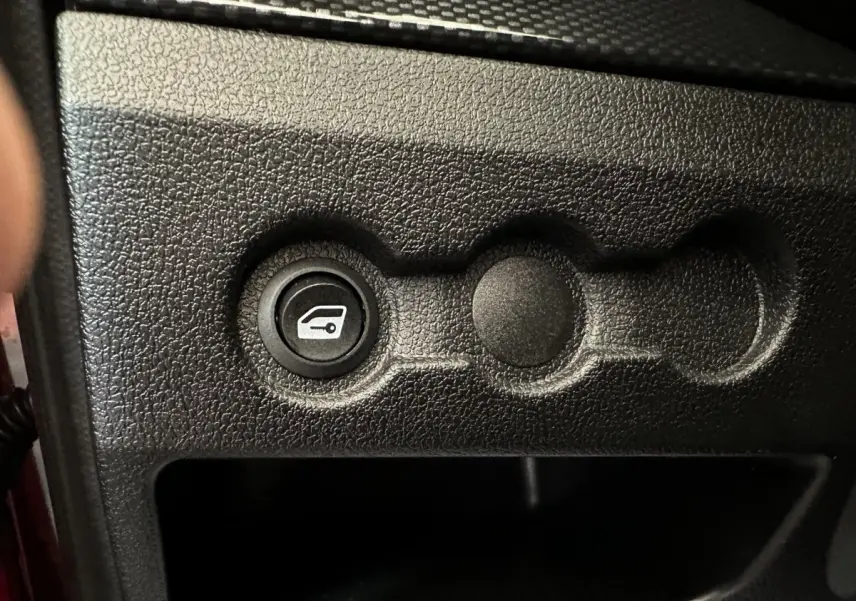 Bouton d'ouverture du coffre sur tableau de bord noir texturé d'une Aixam Ambition rouge 2025.