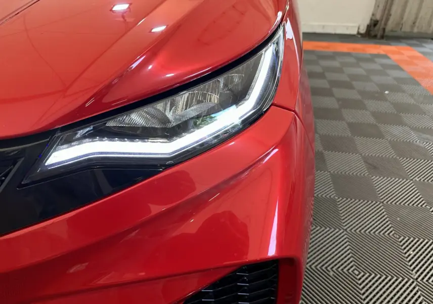 Gros plan sur le phare avant droit allumé d'une AIXAM AMBITION rouge 2025, soulignant ses lignes modernes.