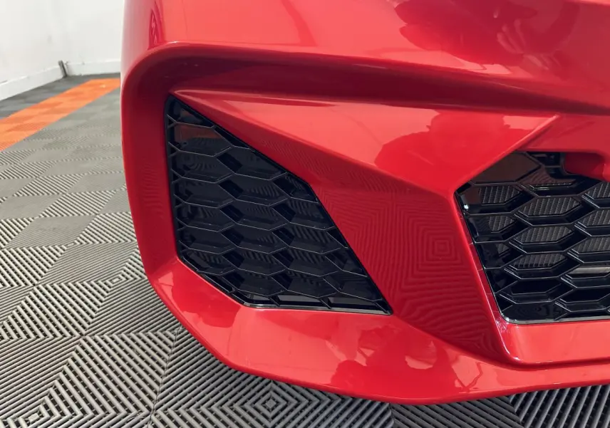 Gros plan sur la calandre avant gauche rouge vif de l'AIXAM AMBITION 0.5 CITY COUPE GTI E5+ 2025 avec grille noire hexagonale.