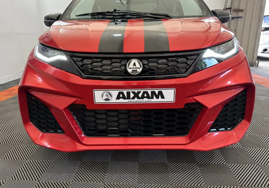 Vue frontale rapprochée de l'AIXAM AMBITION rouge 2025 avec bandes noires et calandre hexagonale marquée.