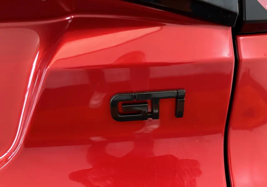 Gros plan sur l’inscription GTI noire sur la carrosserie rouge vif de l’AIXAM AMBITION 0.5 CITY COUPE GTI E5+ côté conducteur.