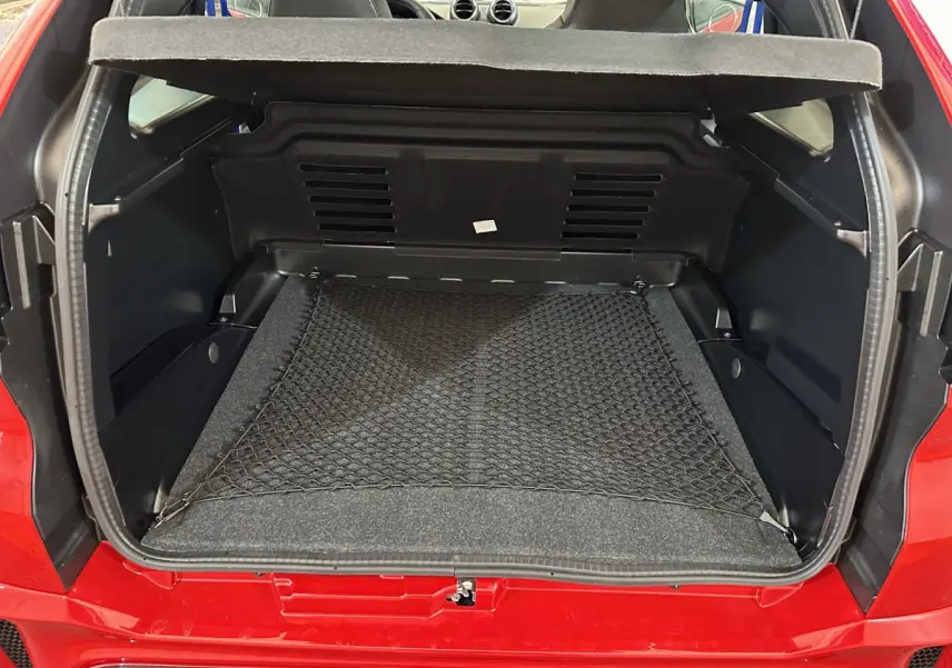Coffre ouvert vu de l'arrière d'une Aixam Ambition rouge 2025 avec filet de rangement et intérieur noir.