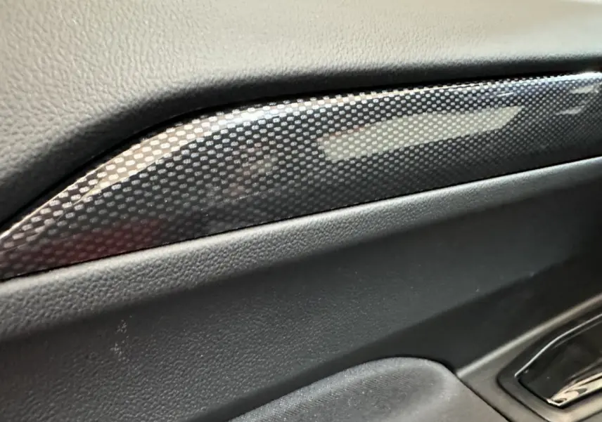 Gros plan sur la garniture intérieure noire avec insert effet carbone de l'AIXAM AMBITION rouge, côté conducteur.