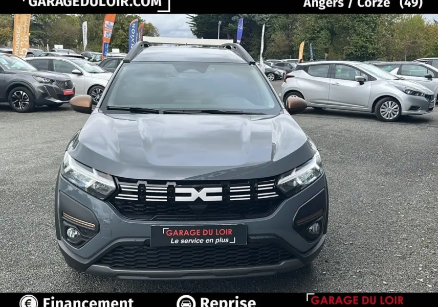 Vue avant d'un Dacia Jogger Extreme+ Hybrid 140 2025 gris foncé avec calandre noire et détails bronze, sur parking extérieur.