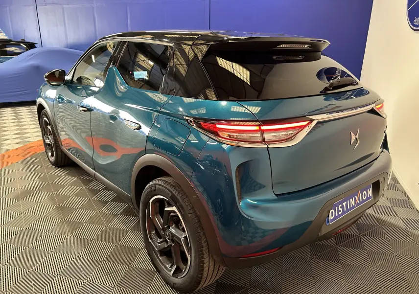 Vue 3/4 arrière droite du DS3 Crossback bleu Millenium avec toit noir et feux arrière allumés dans un showroom.