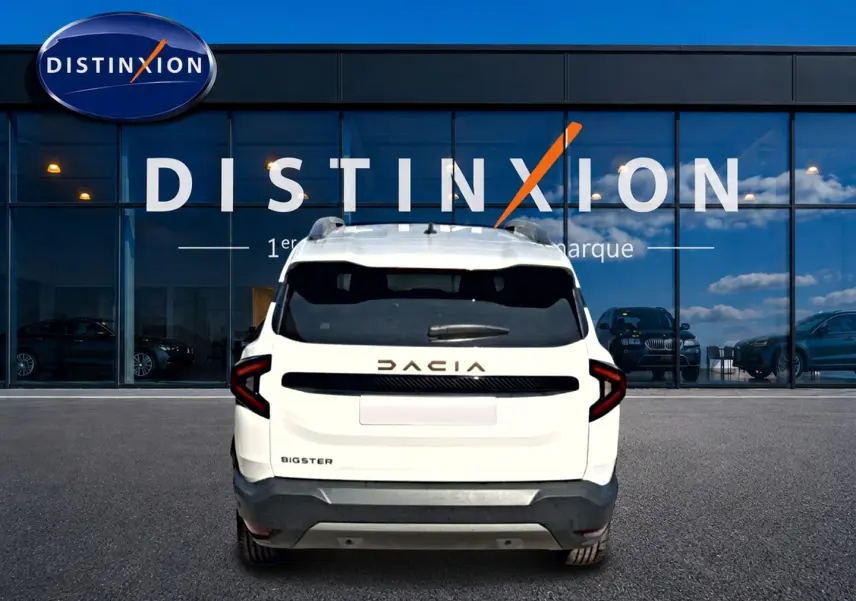 Vue arrière d'un Dacia Bigster blanc 2026 avec barres de toit et feux arrière LED, devant une vitrine Distinxion.