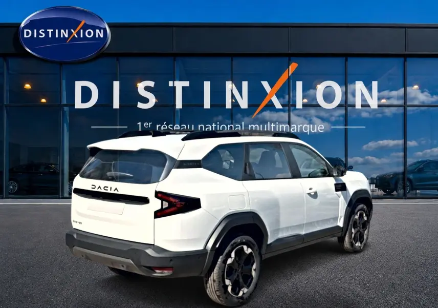 Vue 3/4 arrière droite du Dacia Bigster blanc avec barres de toit noires et jantes alliage distinctives.