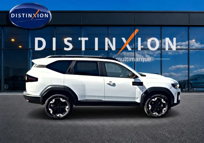 Profil droit du Dacia Bigster blanc 2026 avec jantes noires et toit panoramique devant une vitrine Distinxion.