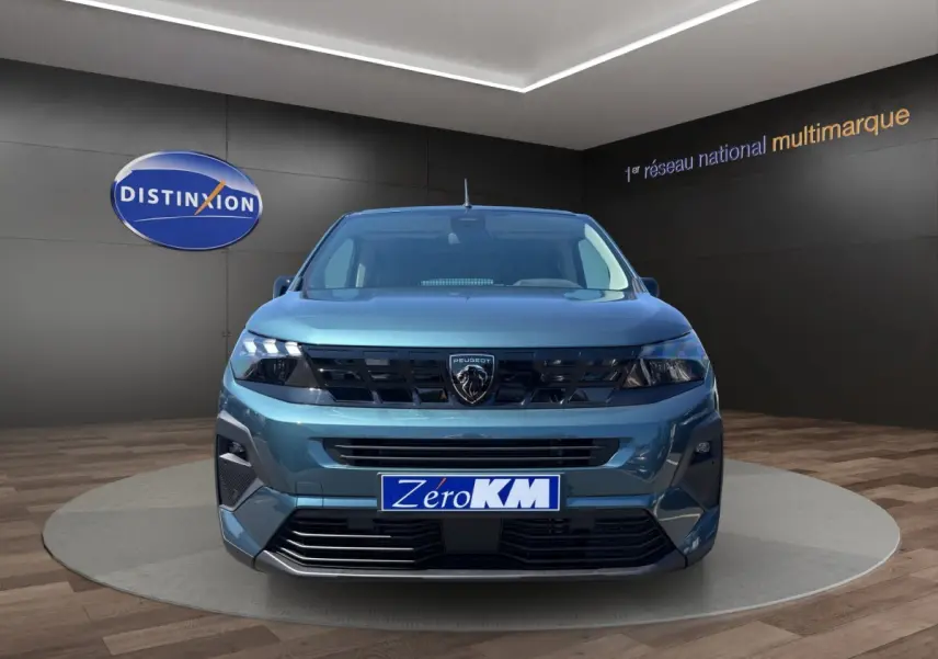 Vue frontale du Peugeot Rifter bleu 2026 avec calandre noire et logo lion distinctif, en showroom.