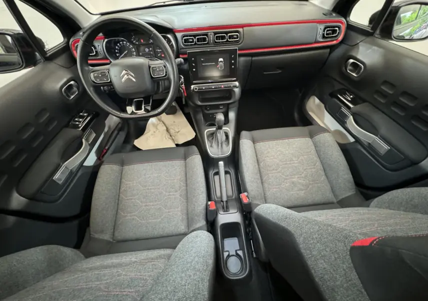 Vue intérieure avant de la Citroën C3 2019, tableau de bord noir avec touches rouges et sièges gris à surpiqûres rouges.
