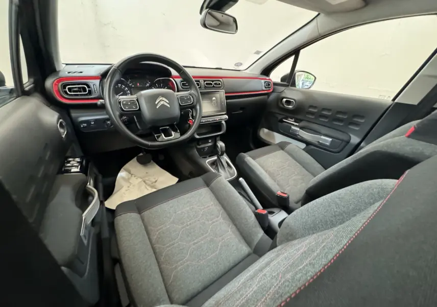 Vue intérieure avant droite de la Citroën C3 noire 2019 avec tableau de bord noir et touches rouges décoratives.