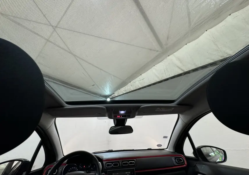 Vue intérieure avant de la Citroën C3 noire 2019, avec toit panoramique et tableau de bord à liseré rouge.