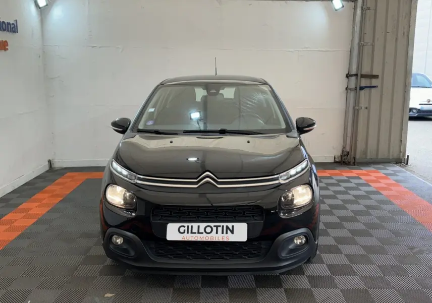 Citroën C3 noire vue de face dans un showroom, avec phares allumés et calandre distinctive.