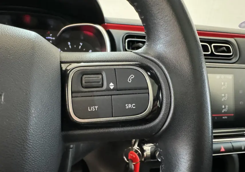 Gros plan sur les commandes gauche du volant cuir noir d'une Citroën C3 noire, avec tableau de bord et écran tactile visibles.