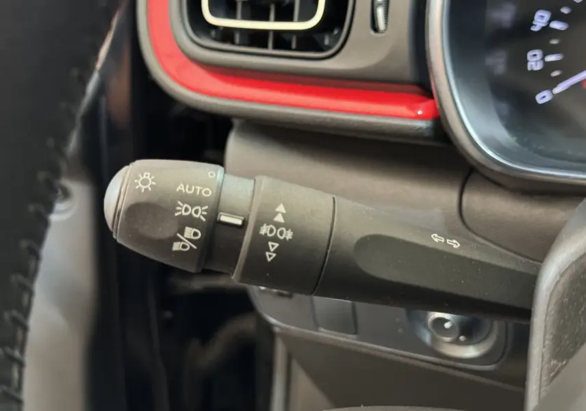 Gros plan sur la commande des phares et clignotants à gauche du volant dans l’habitacle noir et rouge de la Citroën C3 2019.
