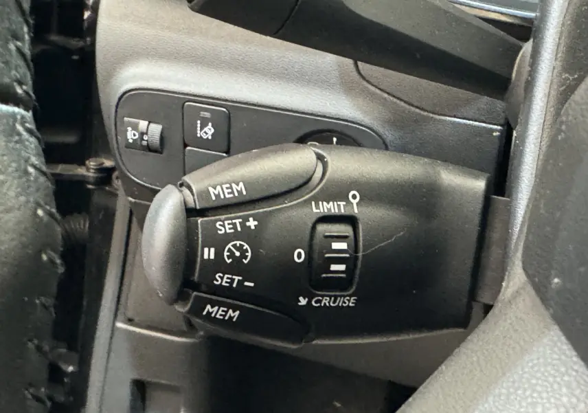 Gros plan sur la commande de régulateur de vitesse noire à gauche du volant d'une Citroën C3 noire de 2019.