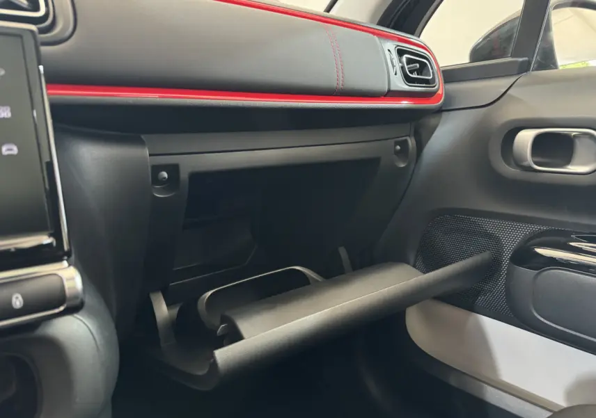 Intérieur côté passager de la Citroën C3 2019 noir, avec boîte à gants ouverte et bandeau rouge décoratif sur le tableau de bord.