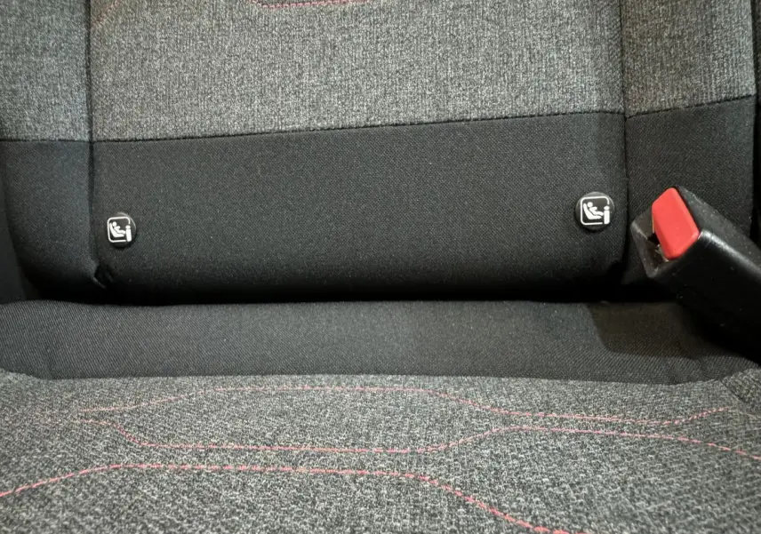 Gros plan sur la banquette arrière grise avec surpiqûres rouges et attaches Isofix visibles d'une Citroën C3 noire.