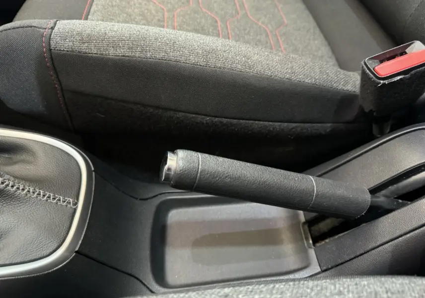 Gros plan sur frein à main en cuir noir et siège tissu gris avec surpiqûres rouges dans Citroën C3 noire 2019.