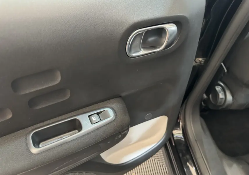 Poignée intérieure et commande de lève-vitre sur la porte arrière droite noire d'une Citroën C3 2019 Shine Business.