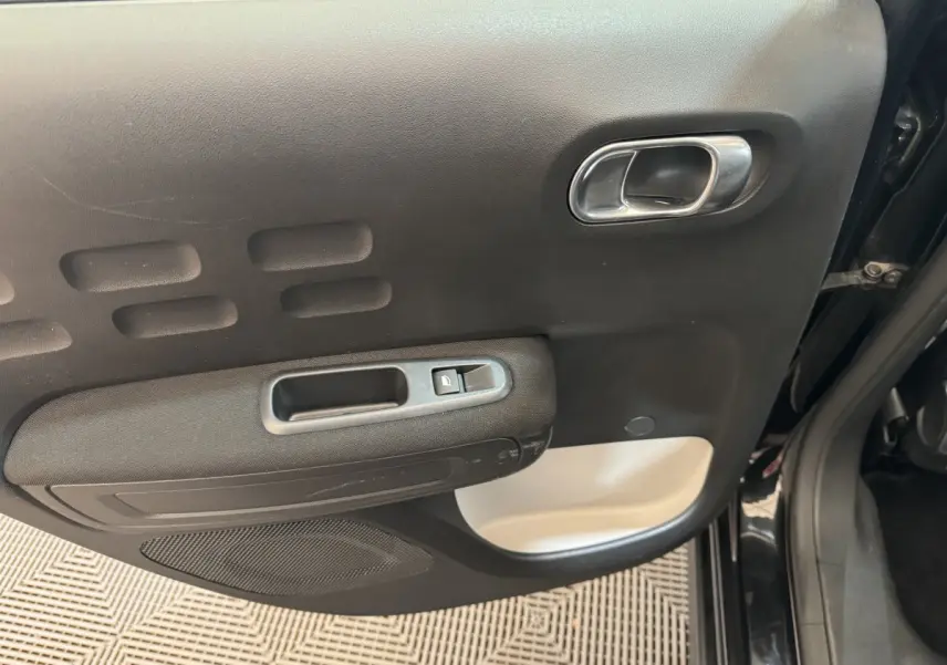 Vue rapprochée de la porte arrière gauche noire de la Citroën C3 avec poignée argentée et commande de fenêtre.