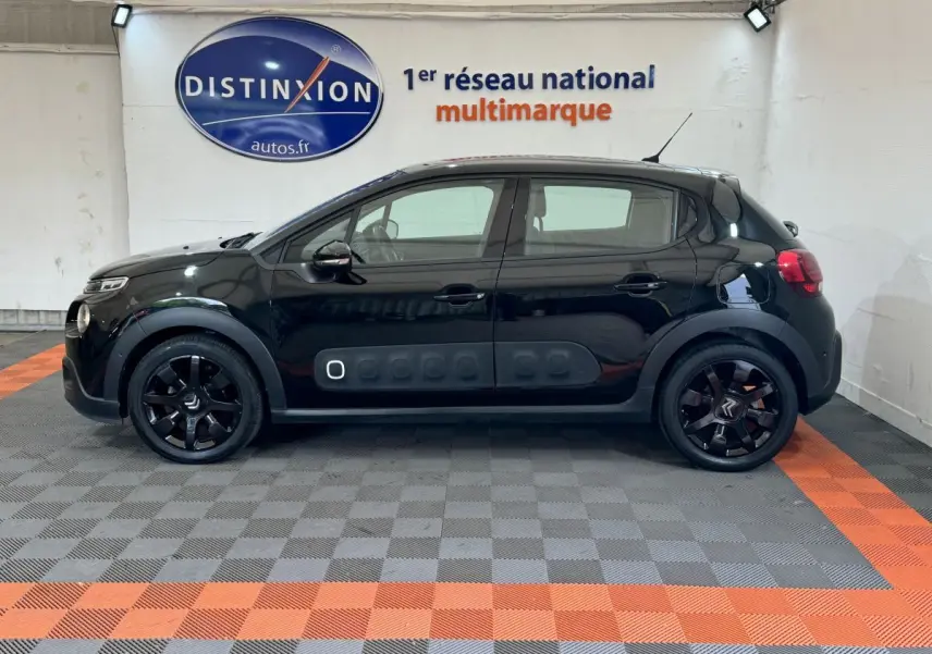 Profil côté gauche d'une Citroën C3 noire 2019 avec protections latérales caractéristiques et jantes noires en intérieur showroom.