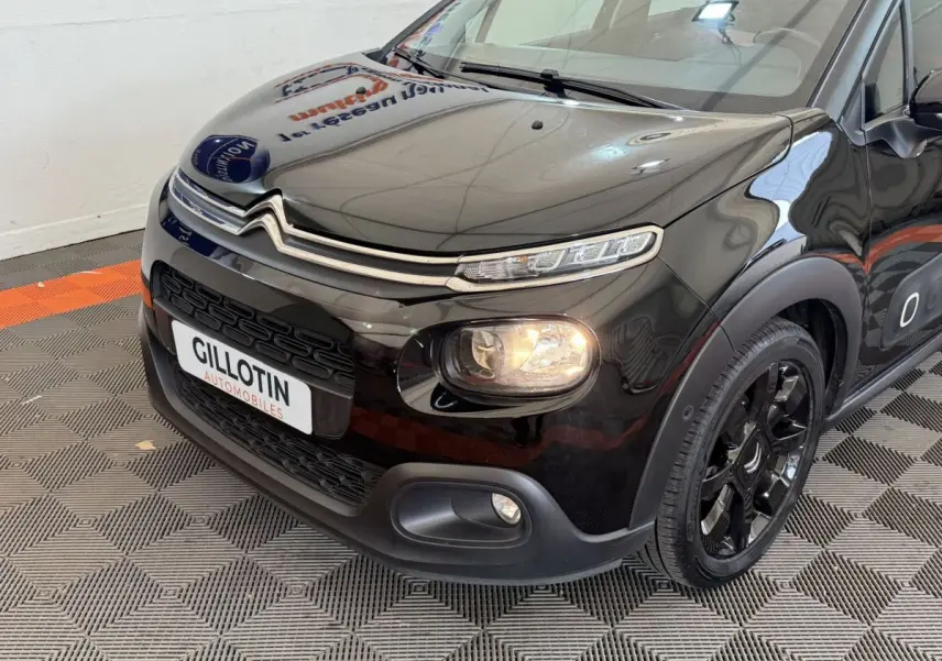 Vue 3/4 avant droite d'une Citroën C3 noire avec phares allumés et jantes noires brillantes.