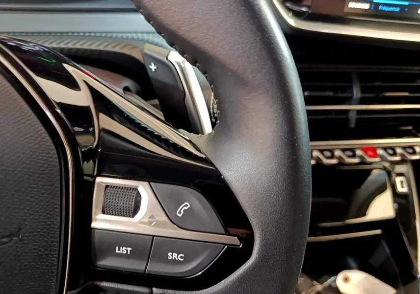 Gros plan sur le volant cuir noir de la Peugeot 2008 2022 avec commandes audio et palettes au volant.