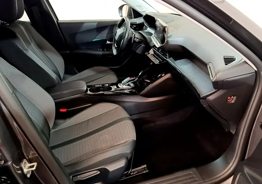 Vue intérieure côté conducteur de la Peugeot 2008 gris foncé, avec tableau de bord moderne et sièges tissu noirs.