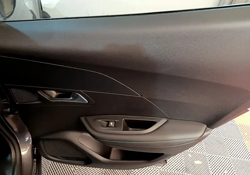 Vue intérieure côté gauche de la porte avant d’un Peugeot 2008 gris foncé, avec poignée et commande de vitre.