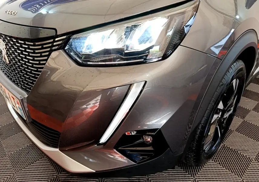 Gros plan sur l'avant droit gris foncé du Peugeot 2008 2022 avec phares LED allumés et jante noire brillante.