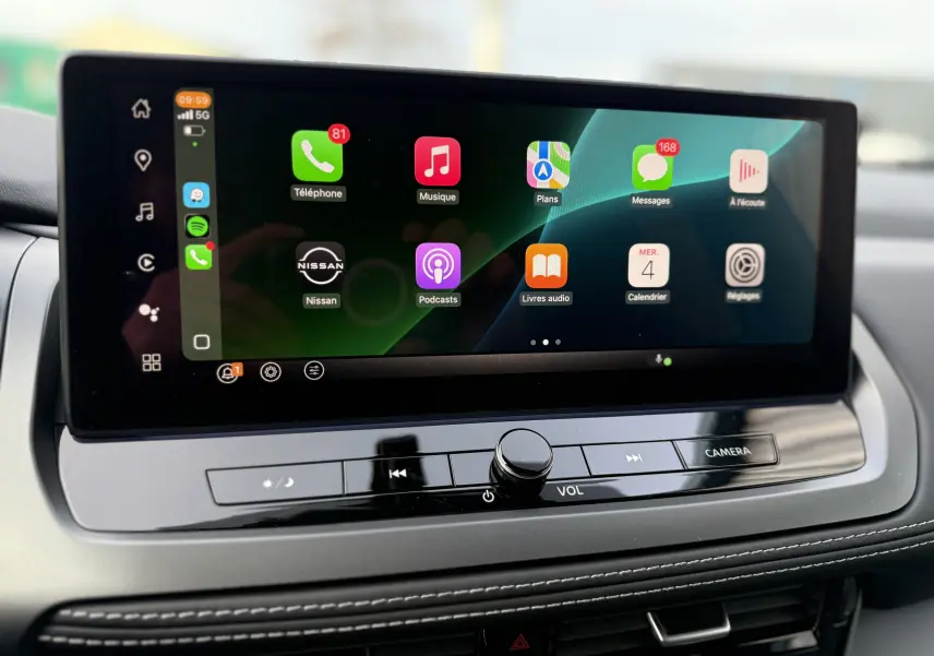 Écran tactile central du Nissan Qashqai 2025 affichant les applications connectées, avec commandes volume et caméra en dessous.