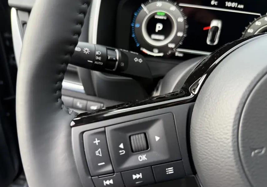 Gros plan sur les commandes multifonctions du volant côté gauche du Nissan Qashqai gris, avec tableau de bord numérique en arrière-plan.