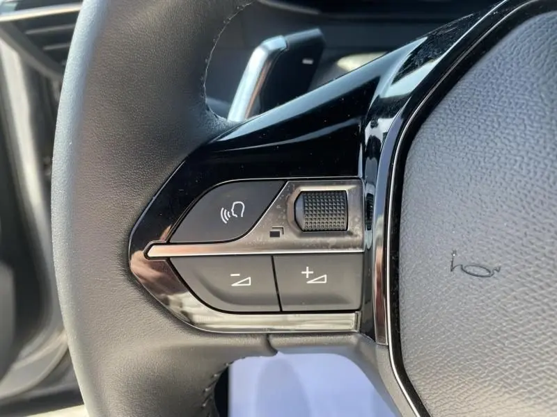 Gros plan sur les commandes de volume et de téléphone sur le volant noir du Peugeot 2008 gris métal 2025.