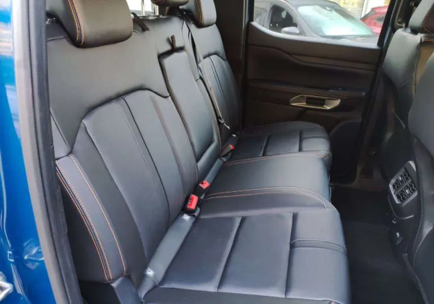 Vue intérieure côté gauche des sièges arrière en cuir noir avec surpiqûres orange d’un Ford Ranger Wildtrak bleu lightning.