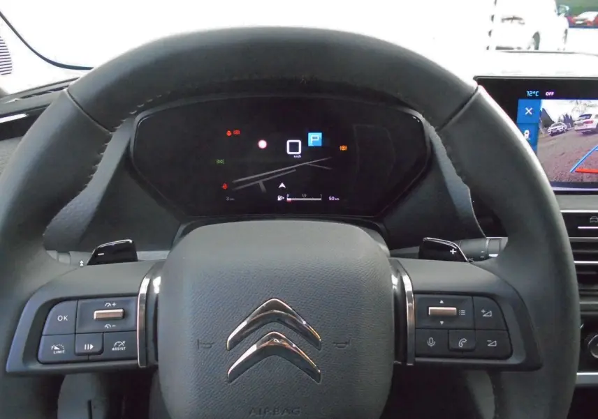 Vue rapprochée du volant noir de la Citroën C5 X avec commandes intégrées et tableau de bord numérique allumé.