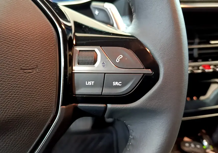 Gros plan sur les commandes gauche du volant cuir noir de la Peugeot 208 gris foncé, boutons LIST et SRC visibles.