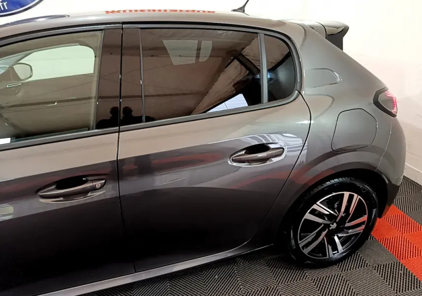 Vue latérale droite d'une Peugeot 208 gris foncé avec jantes alliage et poignées de porte chromées.