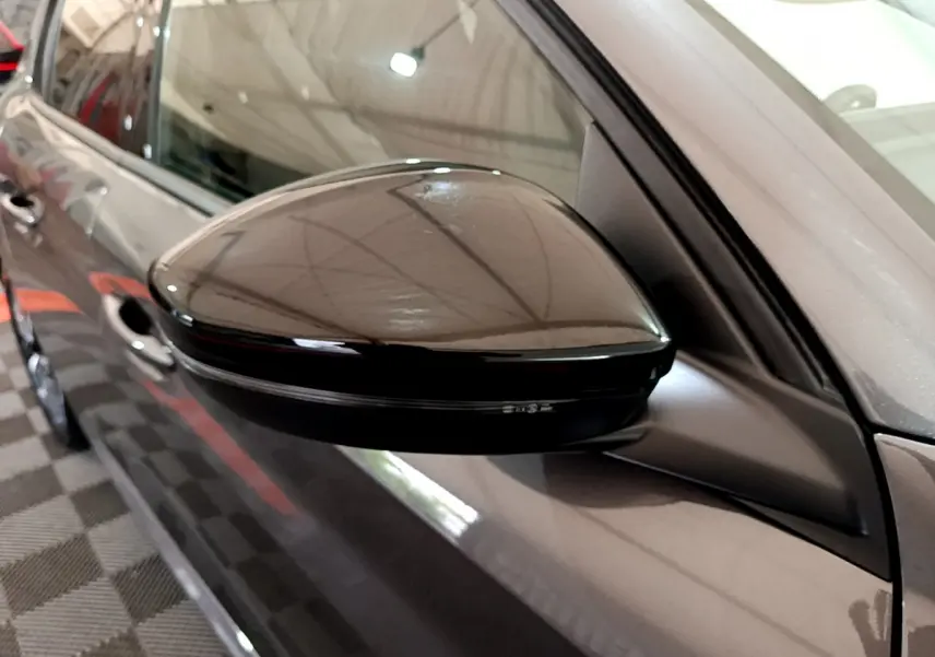 Gros plan sur le rétroviseur droit noir brillant d’une Peugeot 208 gris foncé vue de côté en intérieur.