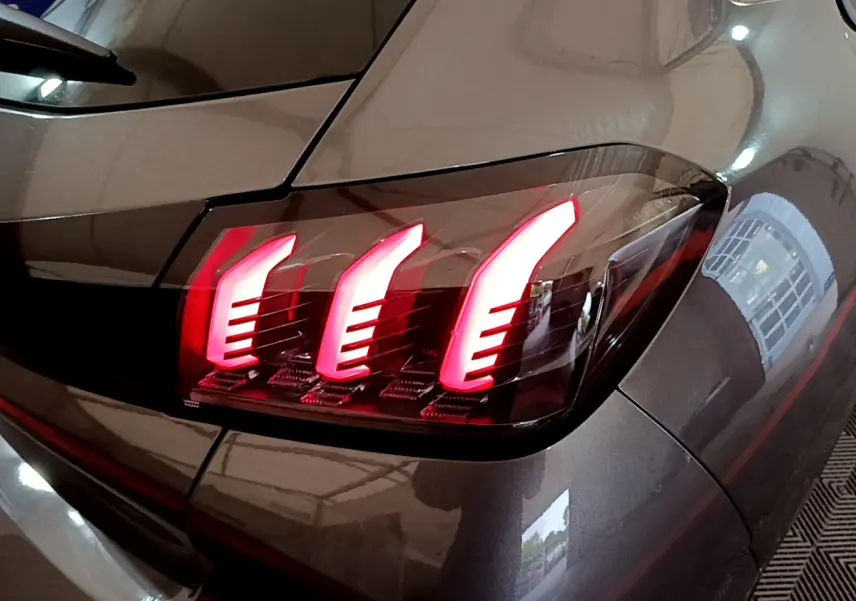 Gros plan sur le feu arrière droit rouge d’une Peugeot 208 gris foncé, soulignant ses lignes modernes et lumineuses.