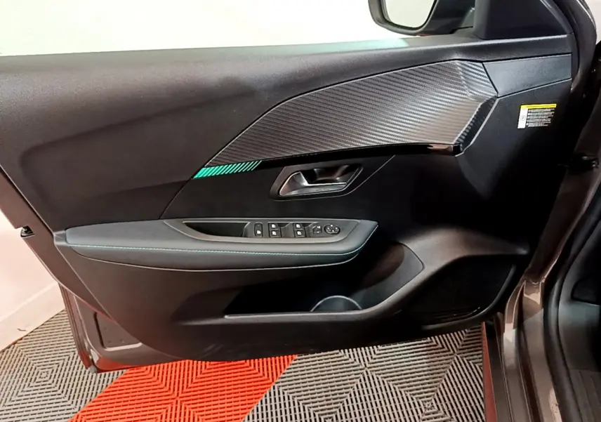 Vue intérieure côté gauche de la porte avant gris foncé de la Peugeot 208 avec insert décoratif carbone et commandes électriques.
