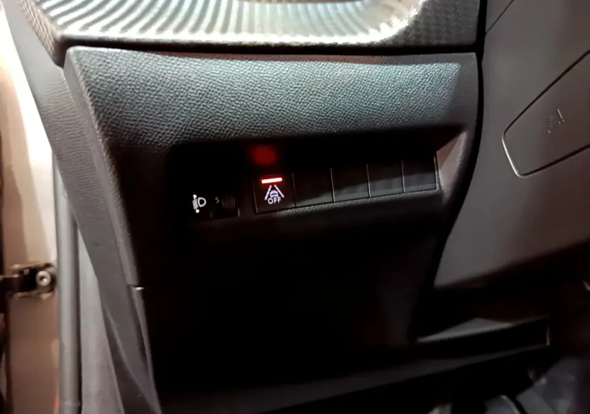 Détail intérieur côté gauche du tableau de bord d’une Peugeot 208 gris foncé, bouton d’aide à la conduite désactivée allumé.